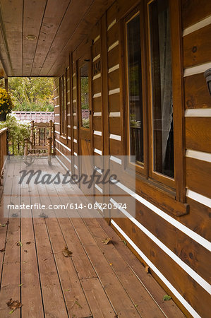 Veranda with rocking chair on facade of rustic Canadian cottage style log home in autumn, Quebec, Canada