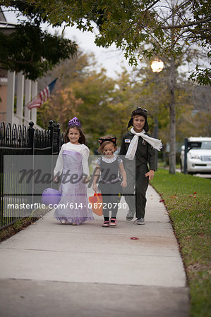 Boy and sisters walking along sidewalk trick or treating