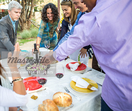 Adult friends helping themselves to food and drink at garden party table
