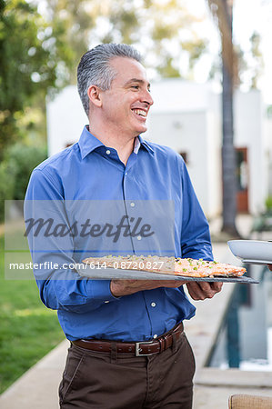Mature man holding fish cuisine on cutting board at garden party