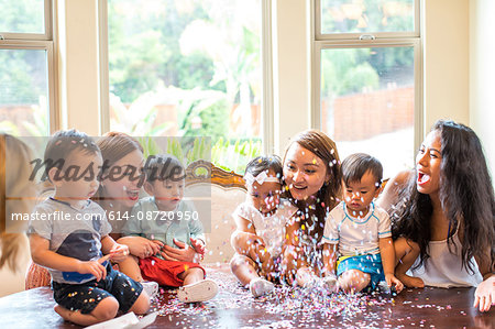 Mothers with baby girl and boys celebrating with confetti on dining room table