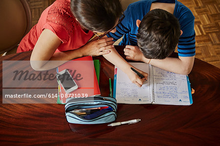 High angle view of mother at dining table helping son with homework