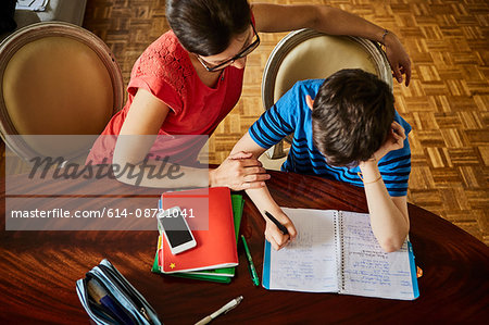 High angle view of mother at dining table helping son with homework
