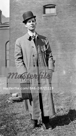 1900s 1910s PORTRAIT MAN STANDING BOWLER HAT LONG WOOL COAT LOOKING AT CAMERA HOLDING LEATHER CASE POSTCARD SIZE KODAK CAMERA