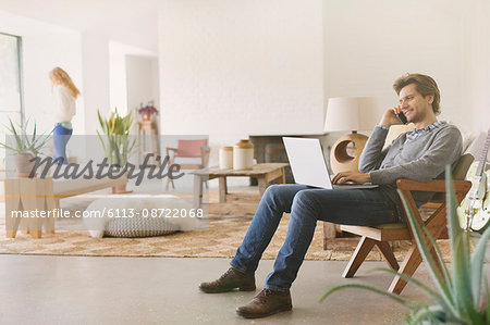 Man talking on cell phone and using laptop in living room