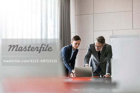 Businessman and businesswoman using laptop in conference room