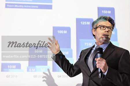 Businessman with microphone speaking at projection screen with bar chart