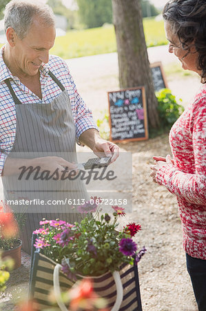 Woman with flowers watching plant nursery worker using credit card machine