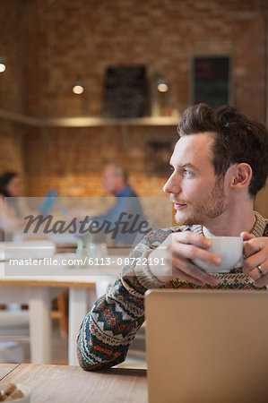Pensive man looking away drinking coffee at laptop in cafe