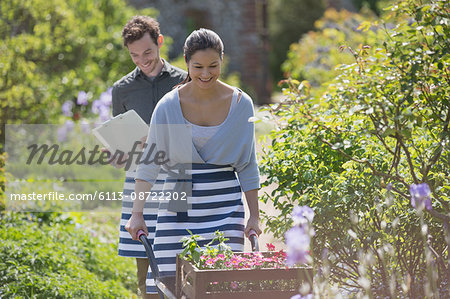 Smiling plant nursery worker pushing wheelbarrow with flowers in sunny garden