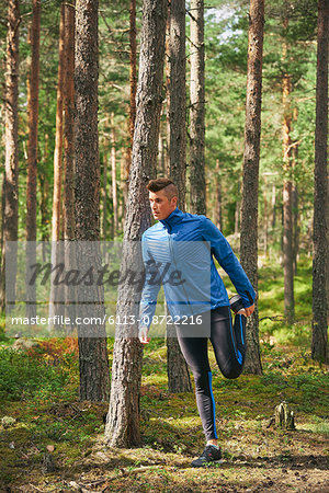 Runner stretching leg at tree in woods