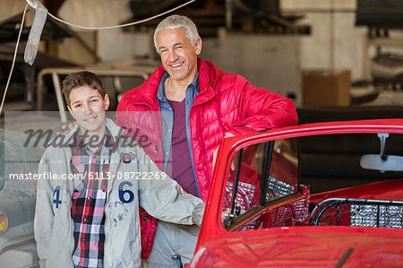 Portrait smiling father and son next to classic car in auto repair shop