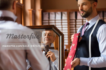 Tailor showing ties to businessman at mirror in menswear shop