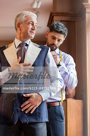 Tailor fitting businessman for suit in menswear shop Tailor fitting businessman for suit in menswear shop