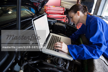 Female mechanic using a digital tablet while servicing car engine at the repair garage