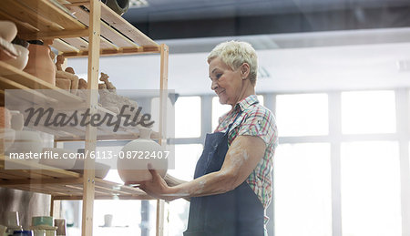 Senior woman placing pottery vase on shelf in studio