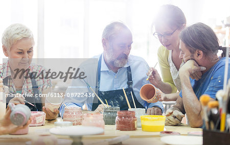 Teacher guiding mature students painting pottery in studio