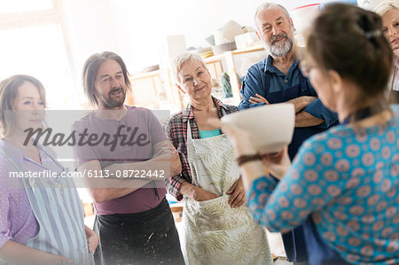 Teacher showing pottery bowl to mature students in studio