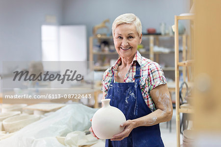 Portrait smiling senior woman holding pottery vase in studio