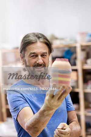 Portrait smiling mature man holding painted pottery vase in studio