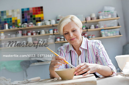 Smiling mature woman painting pottery bowl in studio