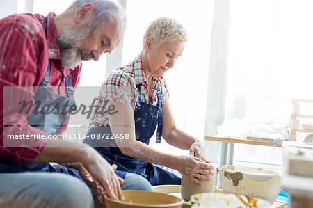 Senior couple using pottery wheels in studio