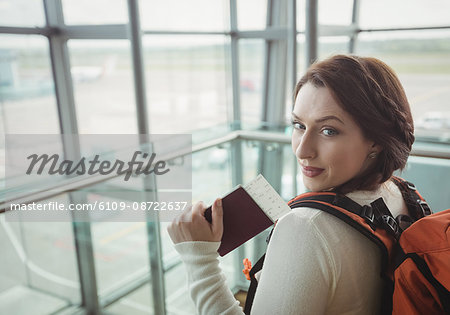 Portrait of woman with passport standing in waiting area at airport terminal