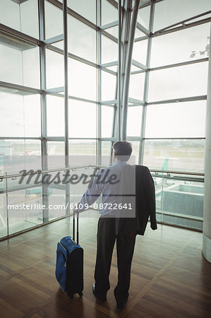 Rear view of businessman with luggage looking through glass window at airport