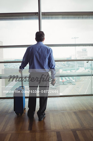 Rear view of businessman with luggage looking through glass window at airport