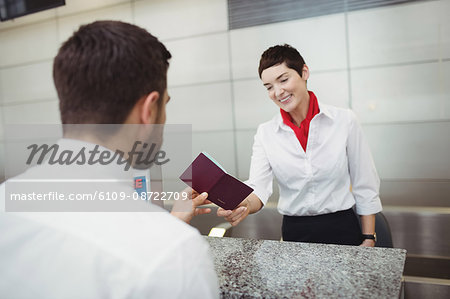 Airline check-in attendant handing passport to passenger at airport check-in counter