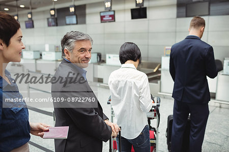 Passengers waiting in queue at a check-in counter with luggage inside the airport terminal