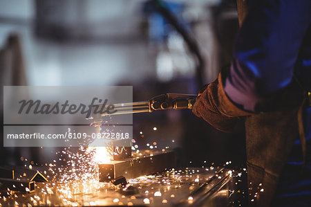 Mid-section of male welder working on a piece of metal in workshop