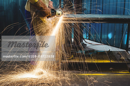 Mid-section of male welder working on a piece of metal in workshop
