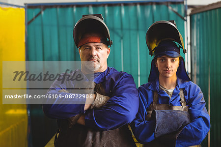 Portrait of male and female welder standing with arms crossed in workshop