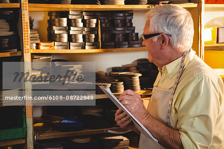 Shoemaker writing on clipboard in workshop