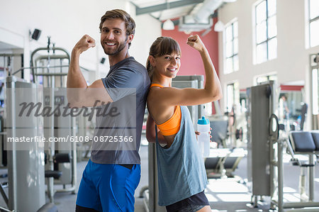 Happy couple standing back to back showing their muscles in a fitness club