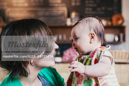 A mother and small baby gazing at each other and smiling, in a coffee shop.