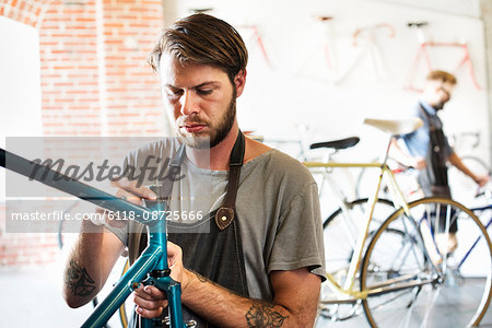 Two men in a cycle repair shop, looking at a bicycle.