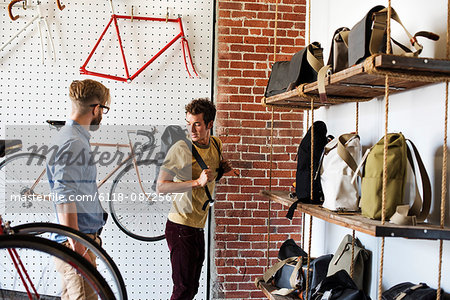 Two men in a cycle repair shop, a client looking at backpacks and bike packs.