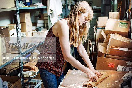 Woman with long blond hair standing in the store room of a shop, wrapping merchandise in brown paper.