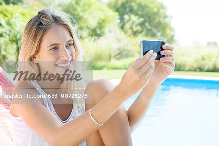 Woman taking a selfie by poolside with smartphone