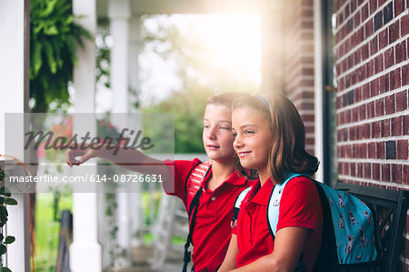 Twin brother and sister sitting on bench pointing, on first day of new school year