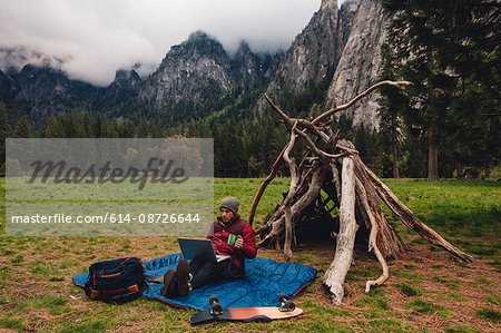 Hiker sitting by den using laptop, Yosemite, California, USA