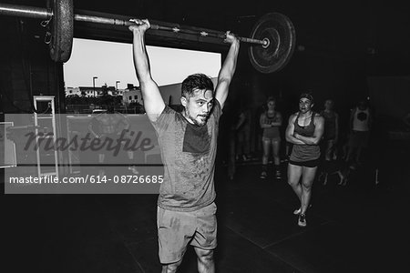 Cross training athlete observing man lifting barbell in gym