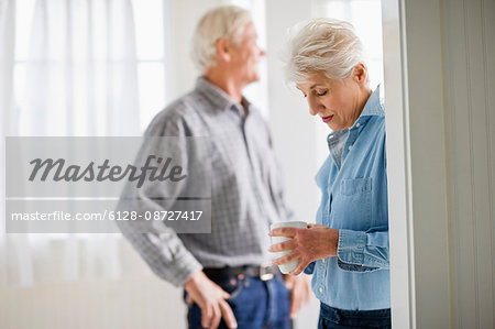 Mature adult couple standing having a drink in a room.