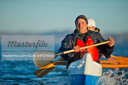 Portrait of a happy middle-aged man paddling an ocean canoe with his friends.