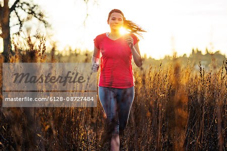 Young woman goes for a countryside run through tall grasses in the late afternoon sunlight.