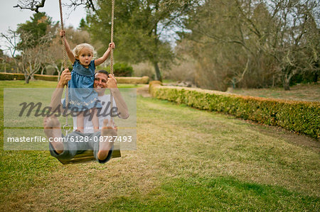 Little girl looks uncertain as she swings on a tree swing with her father.