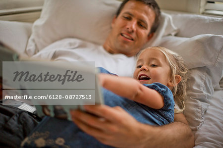 Father lying down reading a book with his daughter.