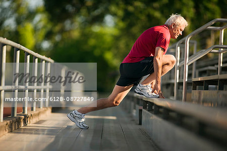 Mature man warming up with stretches on bleachers.